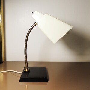 Op de afbeelding: Een witte bureaulamp met een flexibele arm en een zwarte voet. De lampenkap is wit en heeft een kegelvorm.