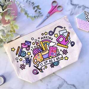 May include: A white canvas zippered pouch with a colorful illustration of art supplies and the text "Making it up as I go".
