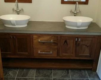 May include: A double vanity bathroom sink with a concrete countertop and wooden cabinets. The sinks are oval shaped and white porcelain. The cabinets have two drawers and two doors.