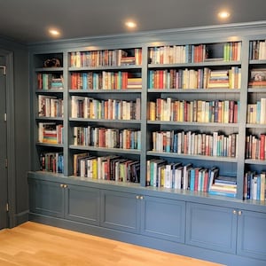 Può includere: Libreria blu integrata con più ripiani pieni di libri di varie dimensioni e colori. La libreria ha una sezione inferiore con armadietti ed è accanto a una porta a vetri.