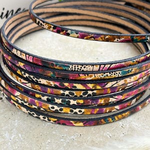 May include: Close-up of a stack of colorful leather cord with a floral and animal print pattern. The cord is black, brown, pink, and white.