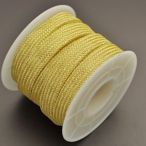 May include: A spool of gold metallic cord, wound tightly on a white plastic spool. The cord is a braided, shiny, metallic thread.