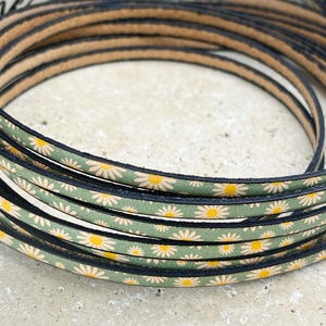 May include: Close-up of a green leather cord with a white daisy pattern. The cord is rolled up and has a black edge.
