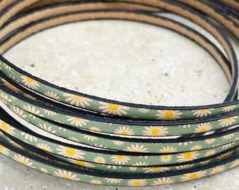 May include: Close-up of a green leather cord with a white daisy pattern. The cord is rolled up and has a black edge.