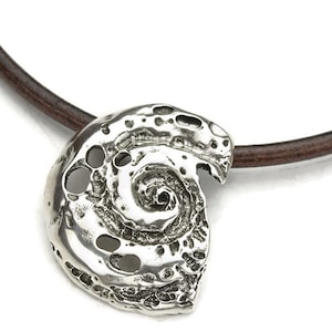 Op de afbeelding: Een zilveren ketting met een hanger in de vorm van een schelp, met een gedetailleerd spiraalvormig ontwerp, hangt aan een bruin leren koord.
