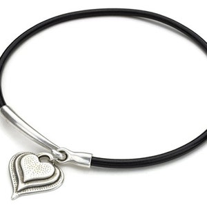 May include: A black leather bracelet with a silver heart charm. The heart charm has a textured surface and a double layered design.