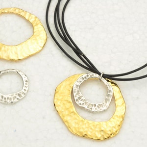 May include: A gold and silver necklace with a hammered metal pendant. The pendant is made of two circles, one inside the other. The necklace is on a black cord.
