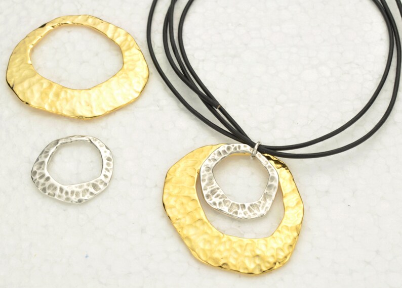 May include: A gold and silver necklace with a hammered metal pendant. The pendant is made of two circles, one inside the other. The necklace is on a black cord.