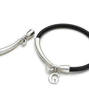 May include: A black leather bracelet with a silver clasp and a silver charm with the letter 'G' on it.