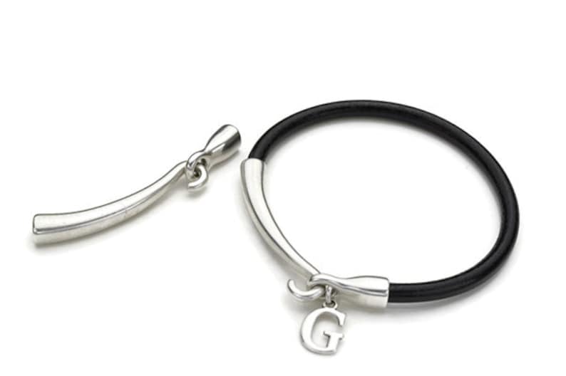 May include: A black leather bracelet with a silver clasp and a silver charm with the letter 'G' on it.