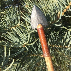 May include: A close-up of a wooden arrow with a grey metal arrowhead and a brown leather wrap around the shaft.
