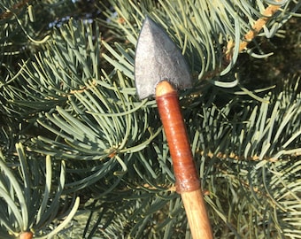 Op de afbeelding: Een close-up van een houten pijl met een grijze metalen pijlpunt en een bruine leren wikkeling rond de schacht.