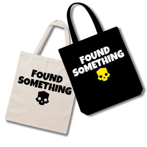 May include: Two tote bags with shoulder straps. One bag is off-white with black text reading FOUND SOMETHING and a black skull icon. The other bag is black with white text reading FOUND SOMETHING and a yellow skull icon below the text.