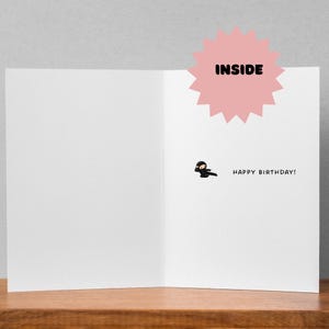 May include: A blank greeting card with a black ninja illustration and the text "Happy Birthday!" inside. The card has a pink starburst with the word "INSIDE" on it.