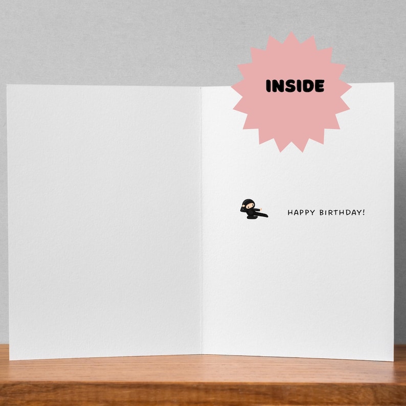 May include: A blank greeting card with a black ninja illustration and the text "Happy Birthday!" inside. The card has a pink starburst with the word "INSIDE" on it.