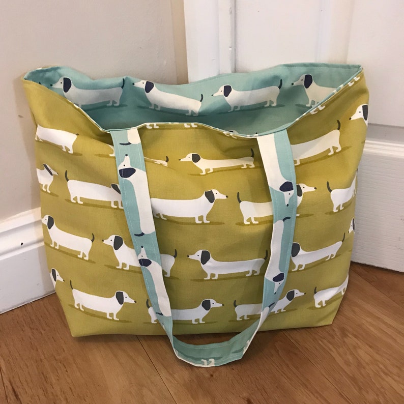May include: A yellow and blue tote bag with a pattern of white dachshunds. The bag has two long straps.
