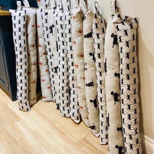 May include: A row of 10 beige doorstops with a black dog print design. The doorstops are lined up on a wooden floor.