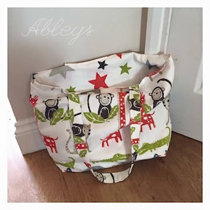 May include: A white tote bag with a colorful print of monkeys, giraffes, crocodiles, and stars. The bag has two long straps.