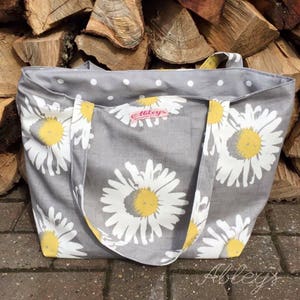 May include: A gray tote bag with white daisy print and white polka dots. The bag has a pink label with the text "Abbey's" on it.