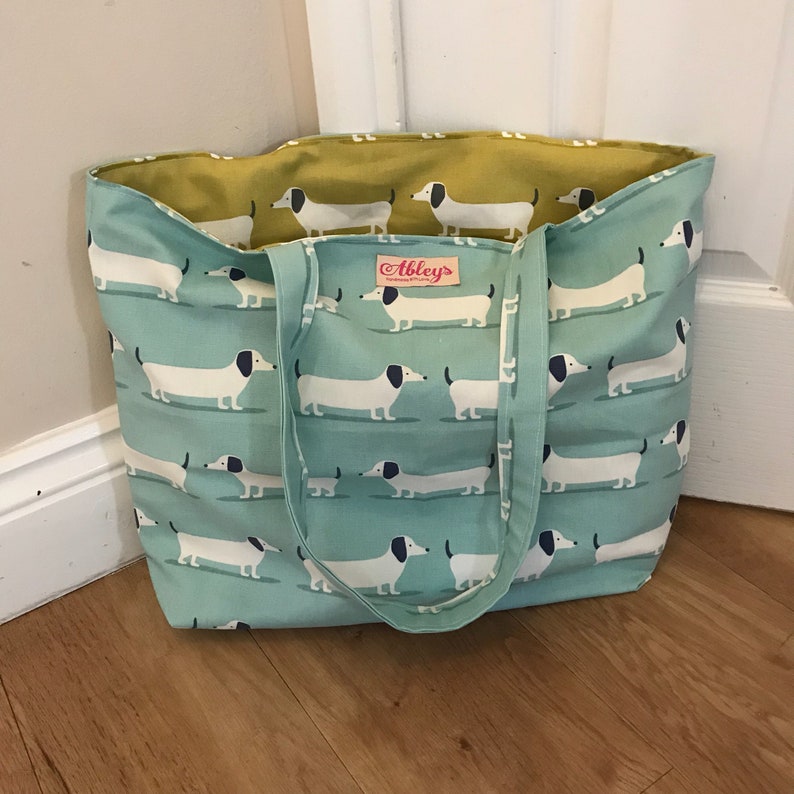 May include: A blue and yellow tote bag with a white dachshund pattern. The bag has a label that says "Abbeys Homewares".