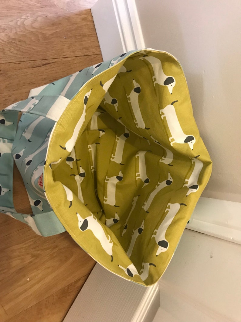 May include: A blue and white striped tote bag with a yellow lining featuring a repeating pattern of white dachshunds with black ears and noses.