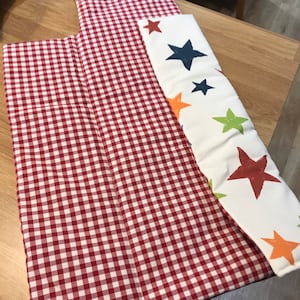 May include: Two fabric panels, one red and white gingham and the other white with colorful stars. The gingham panel is folded in half.