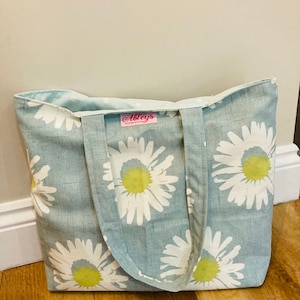 May include: A light blue tote bag with a white daisy print and a pink label that says "Abbeys Handmade With Love".