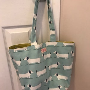 May include: A light blue tote bag with a white and black dachshund pattern. The bag has a yellow lining and a small white label with the text "Abigael" on it.