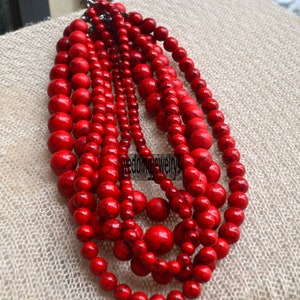 K&ouml;nnte beinhalten: Eine mehrreihige Halskette aus roten Perlen. Die Perlen sind rund und haben eine leicht unregelm&auml;&szlig;ige Form. Die Halskette besteht aus mehreren Perlenreihen, die &uuml;bereinander gelegt sind.