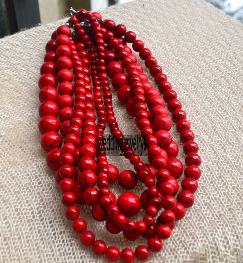 K&ouml;nnte beinhalten: Eine mehrreihige Halskette aus roten Perlen. Die Perlen sind rund und haben eine leicht unregelm&auml;&szlig;ige Form. Die Halskette besteht aus mehreren Perlenreihen, die &uuml;bereinander gelegt sind.