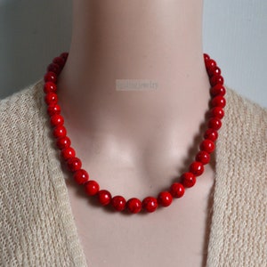 K&ouml;nnte beinhalten: Eine rote Perlenkette aus runden, glatten Steinen. Die Kette befindet sich an einem Mannequin.