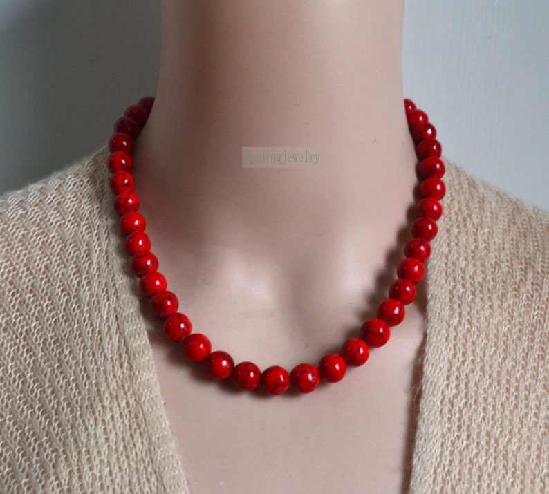 K&ouml;nnte beinhalten: Eine rote Perlenkette aus runden, glatten Steinen. Die Kette befindet sich an einem Mannequin.