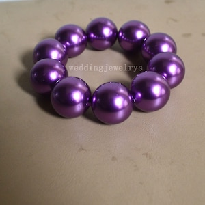 May include: A bracelet made of large, round, shiny, purple beads. The beads are strung together to form a circular shape. The text "weddingjewelrys" is visible on the surface.