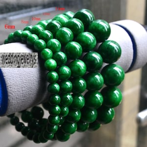 May include: A set of six green jade bead bracelets, each with a different size of beads, ranging from 6mm to 14mm. The bracelets are stacked on top of each other, with the largest beads on the bottom and the smallest beads on the top. The beads are a vibrant green colour and have a smooth, polished finish.