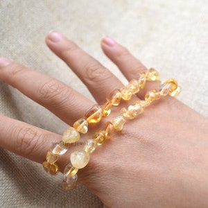 Può includere: Tre braccialetti di citrino giallo impilati su una mano. I braccialetti sono fatti di piccole pietre di forma irregolare.