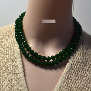 May include: A double strand necklace made of dark green jade beads. The necklace is on a white mannequin.