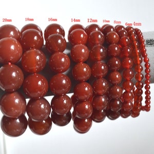 Pode incluir: Um conjunto de 10 pulseiras de pedra de cornalina em vários tamanhos, variando de 4 mm a 20 mm. As pulseiras são exibidas em uma superfície branca.