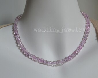 Puede incluir: Un delicado collar compuesto por pequeñas cuentas redondas de color lila claro. Las cuentas están ensartadas para formar un collar tipo gargantilla. El texto "weddingjewelry" es visible en el fondo.