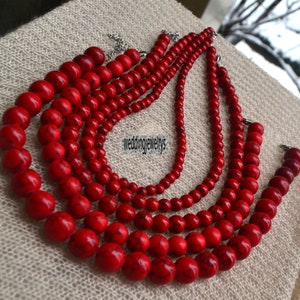 K&ouml;nnte beinhalten: Eine mehrreihige Halskette aus roten Perlen. Die Halskette besteht aus f&uuml;nf Perlenreihen, jede Reihe ist unterschiedlich lang. Die Perlen sind rund und haben eine glatte, polierte Oberfl&auml;che. Die Halskette ist ein wundersch&ouml;nes und elegantes Schmuckst&uuml;ck.