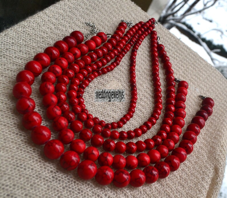 K&ouml;nnte beinhalten: Eine mehrreihige Halskette aus roten Perlen. Die Halskette besteht aus f&uuml;nf Perlenreihen, jede Reihe ist unterschiedlich lang. Die Perlen sind rund und haben eine glatte, polierte Oberfl&auml;che. Die Halskette ist ein wundersch&ouml;nes und elegantes Schmuckst&uuml;ck.