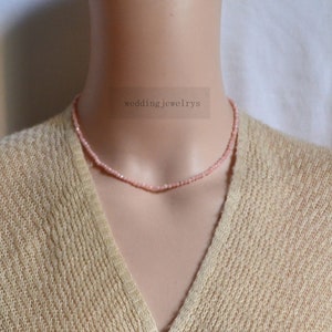 Puede incluir: Un delicado collar de cuentas rosadas en un maniquí. El collar está hecho de pequeñas cuentas redondas y tiene aproximadamente 40 cm de largo. El collar es una pieza de joyería simple y elegante que sería perfecta para cualquier ocasión.