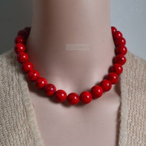 K&ouml;nnte beinhalten: Eine rote Perlenkette aus runden, glatten Steinen. Die Kette befindet sich an einem Mannequin-Hals und ist etwa 46 cm lang.