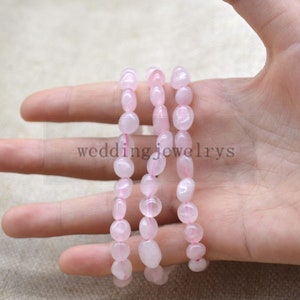 Può includere: Tre fili di perle di quarzo rosa, ogni filo è composto da perle lisce di forma ovale. Le perle sono infilate su un cordoncino elastico trasparente.