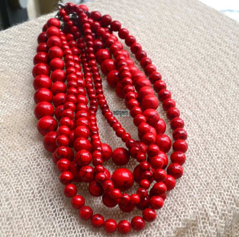 K&ouml;nnte beinhalten: Eine mehrreihige Halskette aus roten Perlen. Die Perlen sind rund und haben eine leicht unregelm&auml;&szlig;ige Form. Die Halskette besteht aus mehreren Perlenreihen, die &uuml;bereinander gelegt sind.