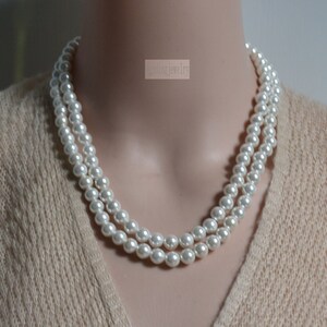 May include: A double strand pearl necklace made of white faux pearls. The necklace is on a mannequin wearing a beige sweater.