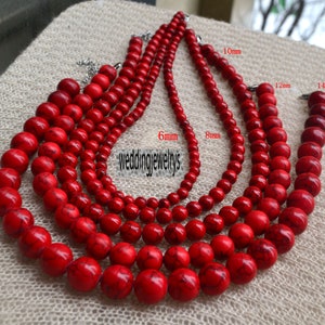 Może przedstawiać: Pięć sznurów czerwonych koralików z kamieni szlachetnych w różnych rozmiarach, od 6 mm do 14 mm. Koraliki są okrągłe i mają gładkie, polerowane wykończenie. Sznurowadła są ułożone w stopniowany wzór, z największymi koralikami na dole i najmniejszymi na górze.