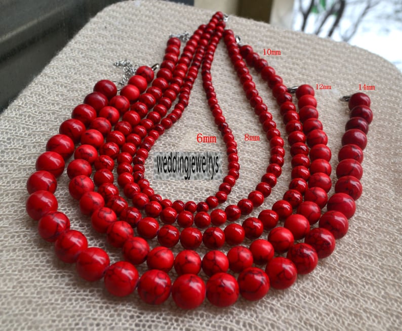 K&ouml;nnte beinhalten: F&uuml;nf Str&auml;nge roter Edelsteinperlen in verschiedenen Gr&ouml;&szlig;en von 6 mm bis 14 mm. Die Perlen sind rund und haben eine glatte, polierte Oberfl&auml;che. Die Str&auml;nge sind in einem abgestuften Muster angeordnet, wobei die gr&ouml;&szlig;ten Perlen unten und die kleinsten Perlen oben liegen.