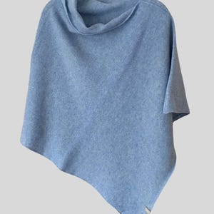 Könnte beinhalten: Ein hellblauer Strickponcho mit einem Rollkragen. Der Poncho hängt an einem Holzbügel.