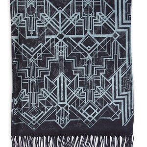 May include: A black scarf with a geometric Art Deco design in light blue. The scarf has a fringe along the bottom edge. The pattern features lines, shapes, and repeating motifs.