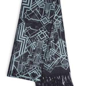May include: A black scarf with a geometric Art Deco design in light blue. The scarf has a fringed edge. The pattern consists of lines and shapes, creating a modern and stylish accessory.